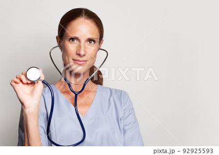 Head shot of woman professiona medical worker wearing blue medical coat holding stethoscope Head shot of woman professiona medical worker wearing blue medical coat holding stethoscope 92925593