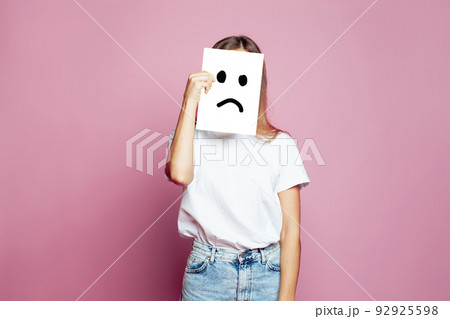 Young woman hiding her face using white paper with sad sign on pink background 92925598