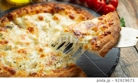 A slice of hot Italian pizza with stretching cheese. Pizza four cheeses with basil. 92929673