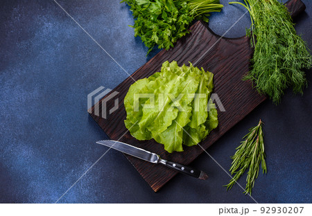 Salad, parsley and dill on a dark cutting board against a blue concrete background Salad, parsley and dill on a dark cutting board against a blue concrete background 92930207