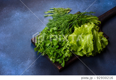 Salad, parsley and dill on a dark cutting board against a blue concrete background Salad, parsley and dill on a dark cutting board against a blue concrete background 92930216