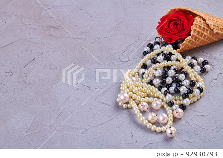 Ice cream cone with pearl necklaces and rose flower. Putty background with copy space. Ice cream cone with pearl necklaces and rose flower. Putty background with copy space. 92930793