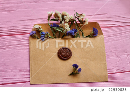 Beige envelope with flowers on pink wooden desk. Attached brown seal. Beige envelope with flowers on pink wooden desk. Attached brown seal. 92930823