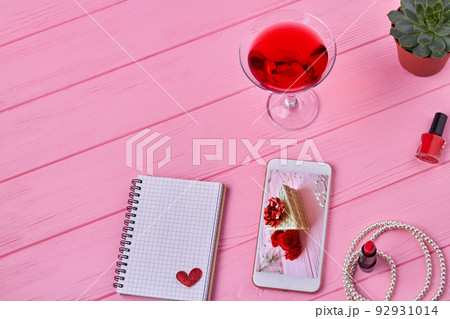 Top view female accessories on pink wooden desk. Smartphone with notepad and cocktail. 92931014