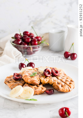 Appetizing croffles with cherries and bananas on a plate on the table. Street food. Vertical view 92931252