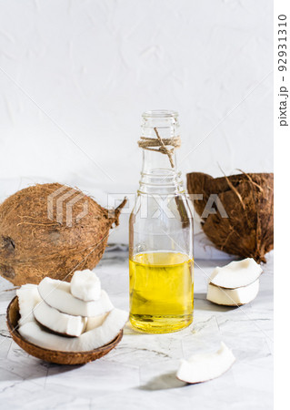 Fresh vegetable coconut oil in a bottle and pieces of coconut on the table. Vertical view Fresh vegetable coconut oil in a bottle and pieces of coconut on the table. Vertical view 92931310