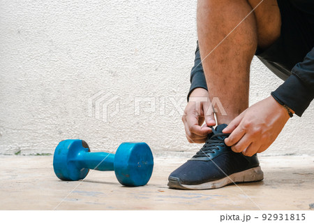 man tying his shoes next to blue dumbbell, before exercising. exercise at home, white background. fitness concept. health concept, space for advertising text man tying his shoes next to blue dumbbell, before exercising. exercise at home, white background. fitness concept. health concept, space for advertising text 92931815