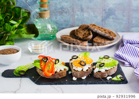 Appetizing bruschetta with feta cheese and vegetables on rye bread on a slate board. 92931996