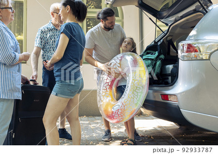 Parents with kid loading bags in trunk, putting baggage in car to leave on holiday vacation journey. Big family with grandparents travelling on summer trip to seaside with inflatable for leisure. 92933787