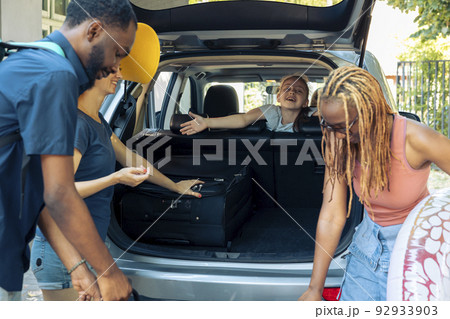 Multiethnic people travelling on summer holiday, loading baggage and inflatable in car trunk to travel to seaside. People preparing to leave on vacation trip with luggage in automobile. Multiethnic people travelling on summer holiday, loading baggage and inflatable in car trunk to travel to seaside. People preparing to leave on vacation trip with luggage in automobile. 92933903