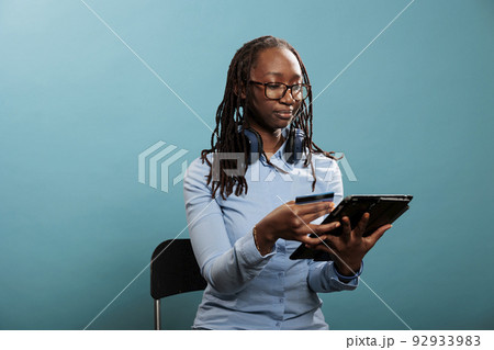 Happy positive attractive woman with modern tablet making a online payment with debit card on shopping store. Young adult person with touchscreen electronic device paying order with credit. 92933983