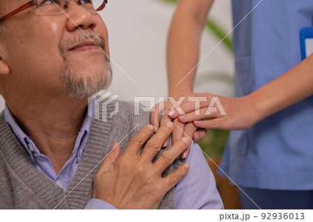 Close up hand of hands of nursing aide holding and patting winkled hand of a patient.Domiciliary care for sick elderly. 92936013