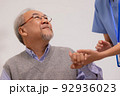 Nursing aide holding and patting winkled hand of a patient.Domiciliary care for sick elderly. 92936023