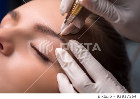 Permanent eyebrow makeup. Cosmetologist applying tattooing of eyebrows. 92937564