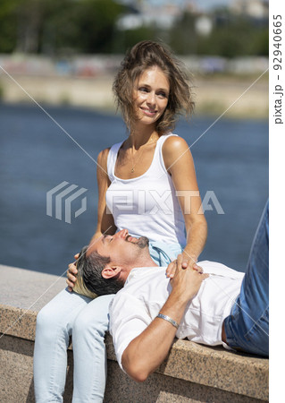 Love and relationships - vertical photo of a man lies on a woman's hips while they having rest on outdoor walking. Love and relationships - vertical photo of a man lies on a woman's hips while they having rest on outdoor walking. 92940665