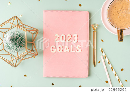 Christmas pink notepad with 2023 goals letters text. Flat lay on green mint table background with planner, cup of coffee, candle, Christmas decoration, notebook and stationery. Top view Desktop Christmas pink notepad with 2023 goals letters text. Flat lay on green mint table background with planner, cup of coffee, candle, Christmas decoration, notebook and stationery. Top view Desktop 92946292
