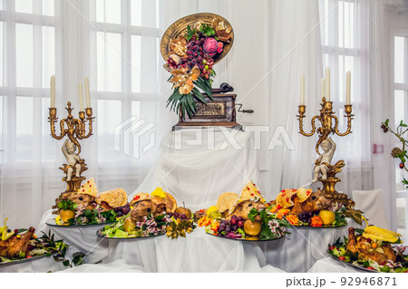 Buffet table with meat snacks, baked pigs in dough with fruit, decorated with candelabra and gramophone 92946871