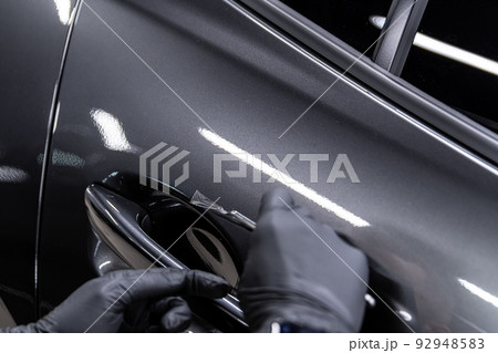 employee of the car detailing studio protects the car body with a protective film 92948583