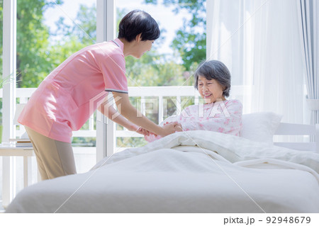 介護 ベットから起きあがるシニアを介助する介護士 介護 ベットから起きあがるシニアを介助する介護士 92948679