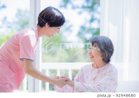 介護 ベットから起きあがるシニアを介助する介護士 介護 ベットから起きあがるシニアを介助する介護士 92948680