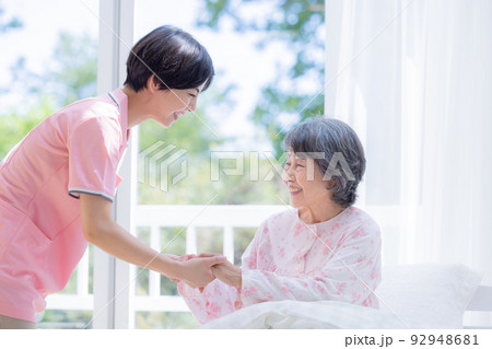 介護　ベットから起きあがるシニアを介助する介護士 92948681