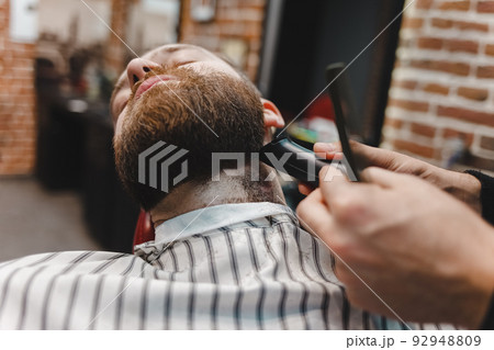 Barber master edging his beard with an electric trimmer machine. 92948809