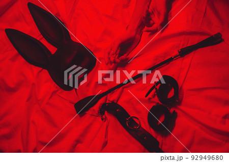 set of BDSM accessories with female hands is lying on the bed. Flogger whip, handcuffs, mask and choker for sex set of BDSM accessories with female hands is lying on the bed. Flogger whip, handcuffs, mask and choker for sex 92949680