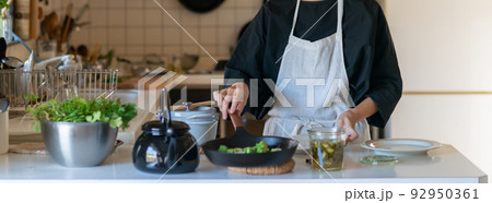 キッチンで料理をするエプロン姿の女性 皿に料理を盛り付ける キッチンで料理をするエプロン姿の女性 皿に料理を盛り付ける 92950361