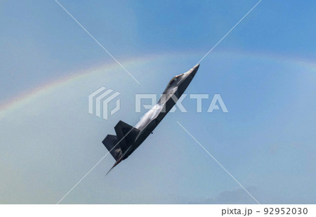 US Airforce F-22 Raptor climbing high with water vapor forming on the wings and a rainbow in the background 92952030