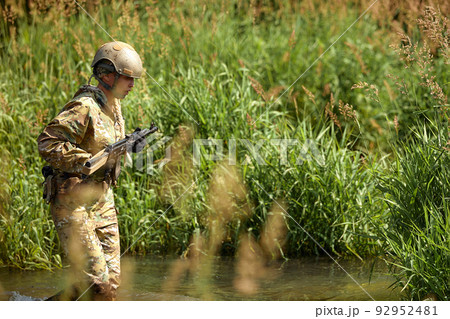Portrait of fit military female holding weapon rifle in hands in river, posing alone. Confident strong athlete lady looking at side seriously. Attractive good-looking female in military gear 92952481