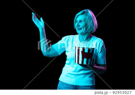 One excited senior woman, modern grandmother holding bucket of popcorn isolated on dark background in neon. Concept of emotions, facial expression, aspiration 92953027