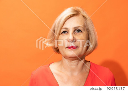 Half-length portrait of beautiful middle age woman with blond hair posing isolated on orange color background. Concept of emotions, facial expressions Half-length portrait of beautiful middle age woman with blond hair posing isolated on orange color background. Concept of emotions, facial expressions 92953137