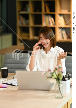 Pretty young entrepreneur having phone conversation, negotiations with business partner on mobile phone 92953356