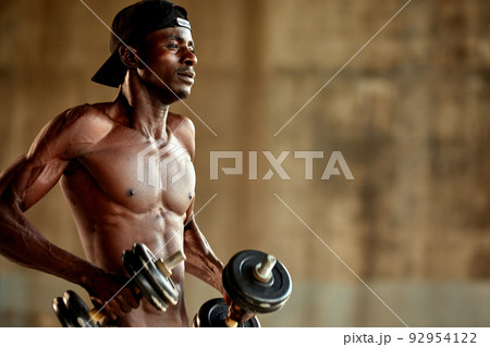 Attractive african american man smiling and doing exercise with dumbbells. Attractive african american man smiling and doing exercise with dumbbells. 92954122