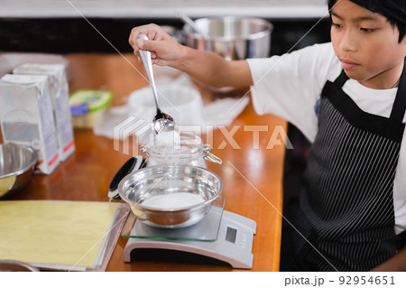 Young boy measuring ingredient for baking in kitchen. Young boy measuring ingredient for baking in kitchen. 92954651
