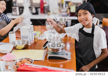 Young boy and his mum preparing ingredient for baking cake in kitchen. Young boy and his mum preparing ingredient for baking cake in kitchen. 92954652