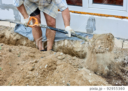 Digging trench for laying cable, construction worker uses shovel to take out soil. 92955360
