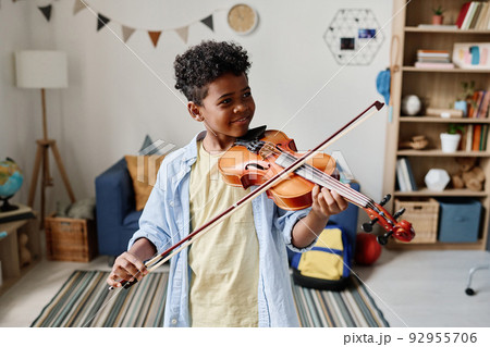 African boy playing violin during lesson while standing in his room at home 92955706