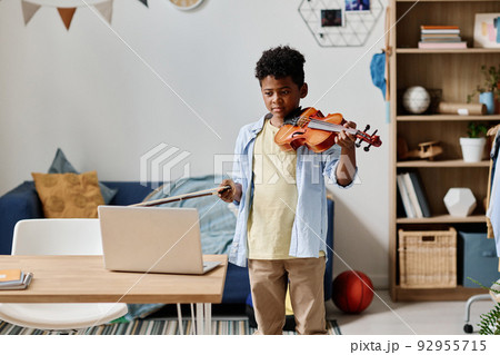 African child standing in front of laptop and learning to play violin during online lesson African child standing in front of laptop and learning to play violin during online lesson 92955715