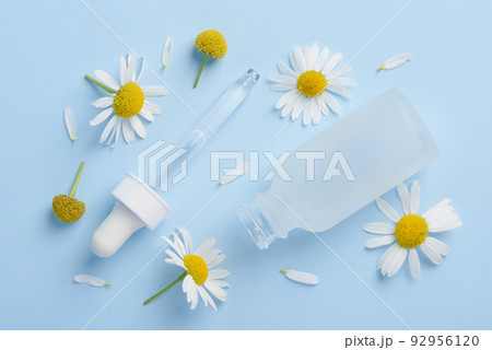 Cosmetic skincare serum dropper and bottle with chamomile flowers and petals on blue Cosmetic skincare serum dropper and bottle with chamomile flowers and petals on blue 92956120