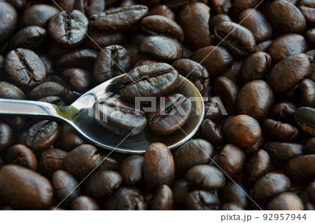Close up of coffee beans on small silver spoon. Food and beverage concept. Close up of coffee beans on small silver spoon. Food and beverage concept. 92957944