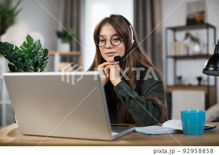 Young caucasian woman in headset talking during video chat on modern laptop. Young caucasian woman in headset talking during video chat on modern laptop. 92958858