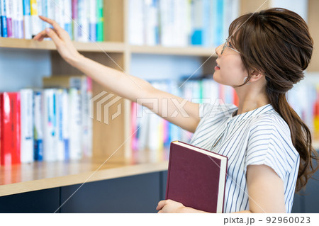 本棚から本を選ぶ若い女性 本棚から本を選ぶ若い女性 92960023