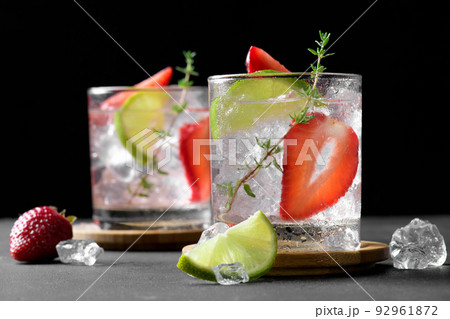 Two glasses with summer strawberry soda drink or mojito with strawberry, ice cubes and lime on dark background 92961872
