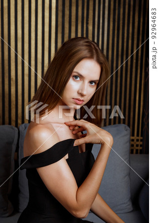 Young caucasian woman in evening dress sitting on couch at home looking at camera 92964683