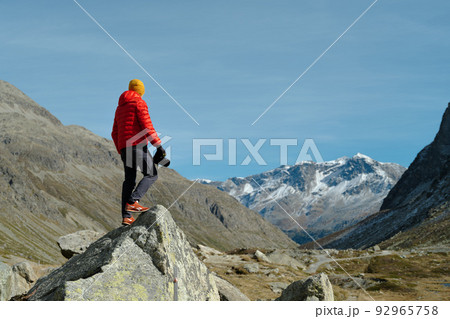 Back view of a tourist man in red jacket and camera standing with a view on Julier Pass, Switzerland 92965758