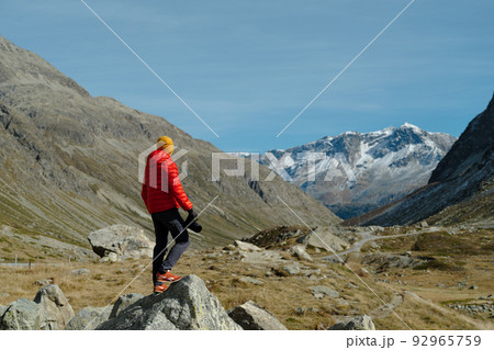 Back view of a tourist man in red jacket and camera standing with a view on Julier Pass, Switzerland Back view of a tourist man in red jacket and camera standing with a view on Julier Pass, Switzerland 92965759
