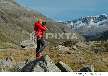 Back view of a tourist man in red jacket and camera standing with a view on Julier Pass, Switzerland 92965760