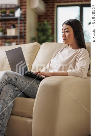 Woman of asian ethnicity working in home office using laptop computer technology web online remote internet job searching social media browsing news reading gossip Woman of asian ethnicity working in home office using laptop computer technology web online remote internet job searching social media browsing news reading gossip 92968957