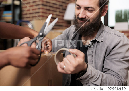 Husband and wife cutting adhesive tape with scissors to move in rented apartment flat, using sticky roller to pack furniture for storage transportation. Moving day for new beginnings. Close up. 92968959